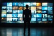 © K'kriang Krai - A man in a suit stands and watches television on a large screen wall with multiple screens, against a media news background.
