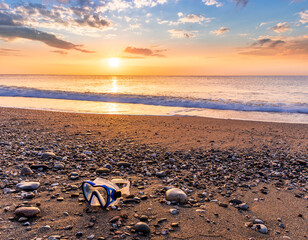 ocean cloudy morning landscape with diving mask on sea coast on foreground, sand of a beach, blue sea with surf and waves and cloudy sunset or sunrise on background