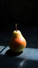 A single, ripe pear sits on a dark surface, illuminated by a ray of sunlight.