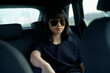 © Connect Images - Woman in sunglasses sitting in the backseat of a car, with a calm expression.