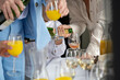 © Connect Images - Waiter pouring champagne into glasses at a social event with guests holding drinks.