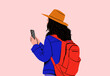 © Connect Images - Adult with a backpack looking at a smartphone, wearing a blue jacket and orange hat against a pink background.