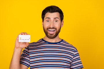 Canvas Print - Portrait of impressed guy with bristle wear striped t-shirt presenting debit card astonished staring isolated on yellow color background