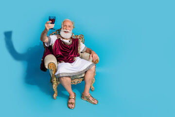 Full body portrait of rich wealthy ancient roman citizen sit throne hold wine glass empty space isolated on blue color background