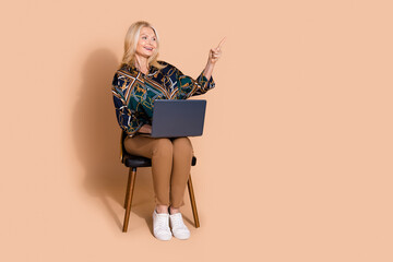 Sticker - Photo of blonde mature age business woman sitting office chair with laptop direct finger ecommerce ad isolated on beige color background