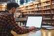 © SKIMP Art - Close-up of a young man sitting at a desk, using a laptop with a blank white screen A library is visible in the background, serving as a mockup template for an online learning website Generative AI