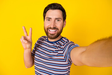 Canvas Print - Portrait of optimistic guy with bristle wear striped t-shirt making selfie showing v-sign symbol isolated on yellow color background