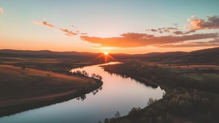 Wall Mural - A serene sunset over a winding river, framed by hills and open fields, creating a picturesque landscape of natural beauty.