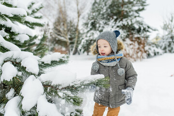 Wall Mural - Adorable little boy having fun on snowy winter day. Cute child wearing warm clothes playing in a snow.