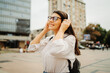 © Dusan - Young caucasian woman listening to music or audio book in the city