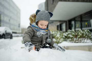 Wall Mural - Adorable little boy having fun in a city on snowy winter day. Cute child wearing warm clothes playing in a snow.