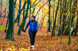 © Jacek Chabraszewski - Middle-aged woman dressed sporty in blue jacket and black pants, cap and glasses training in forest full of fallen leaves in autumn weather. Front view
