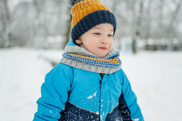 Wall Mural - Adorable little boy having fun on snowy winter day. Cute child wearing warm clothes playing in a snow.