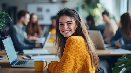 a young woman in a yellow sweater is sitting at a desk with a laptop and a coffee mug, smiling and l