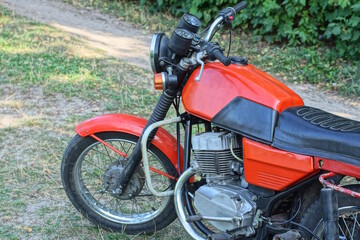 one old red black motorcycle stands on the ground and green grass on the summer street