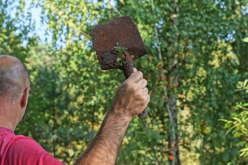 one criminal aggressive man swings rusty iron shovel in hand over head in summer forest against green vegetation background