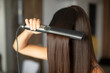 © Home-stock - Young brunette woman straightening her glowing healthy hair using modern iron hair straightener at home, closeup