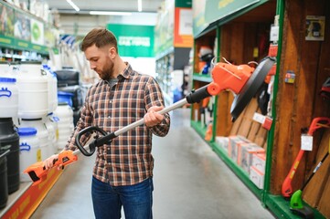 Wall Mural - a young man in a gardening equipment store chooses an electric trimmer for mowing lawn grass