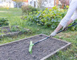 © Sergei - A woman is sweeping a garden bed with a green and black rake