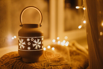 Wall Mural - Glowing christmas lantern with golden lights on cozy knitted sweater on frosty window sill in eve. Atmospheric magical still life. Merry Christmas and Happy Holidays! Winter wallpaper