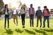 © FotoPush/peopleimages.com - School kids, jumping and playing outdoor on grass with backpack for recess, learning break and fun activity. Students, friends and diversity group on lawn for playground game, education and energy