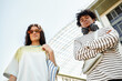 © Seventyfour - Low angle shot of teenage multiethnic boy and girl standing outside in city looking down at camera while posing against bright summer sky, copy space