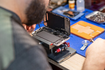 Aufkleber - A technician carefully repairs a phone, focusing on battery replacement and intricate components in a busy workshop setting