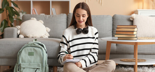 Poster - Beautiful happy female student with stack of books, backpack and headphones studying on floor at home