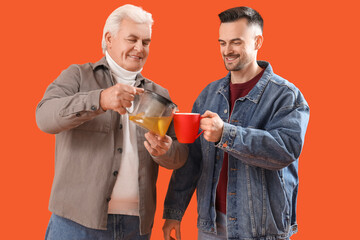 Wall Mural - Young man with his father pouring lemon tea on orange background