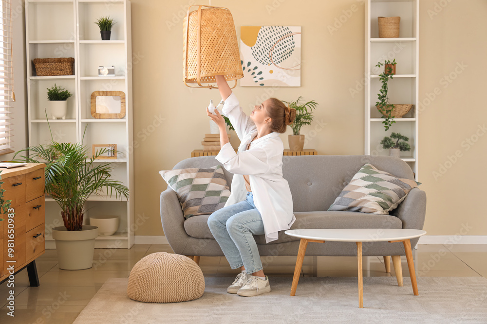 Young woman screwing light bulb into wicker lamp at home