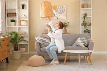 Wall Mural - Young woman screwing light bulb into wicker lamp at home