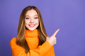 Sticker - Portrait of youth charming blonde hair cute happy smile girl in orange turtleneck pointing finger billboard isolated on violet color background