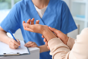 Young man with pain in his wrist visiting doctor at hospital, closeup