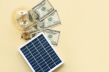 Portable solar panel with dollar banknotes and light bulb on yellow background. Green Energy concept