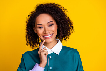 Poster - Portrait of toothy beaming nice girl with wavy hairstyle wear teal shirt holding finger on chin isolated on yellow color background