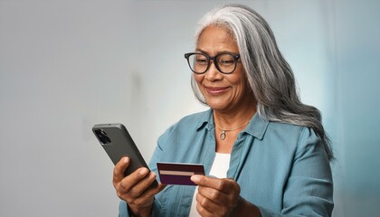 Older mature senior woman holding a phone and a credit card using technology to pay purchases online.