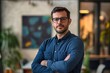 © ImronDesign - Portrait, glasses and business man with arms crossed in startup office for pride in career or job. Creative, face and confident professional entrepreneur, copywriter and employee coworking , ai