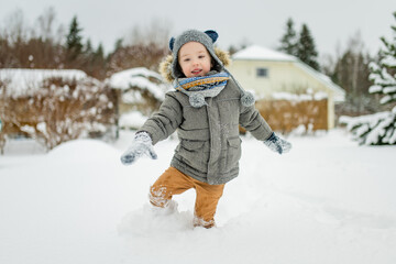 Wall Mural - Adorable little boy having fun on snowy winter day. Cute child wearing warm clothes playing in a snow.