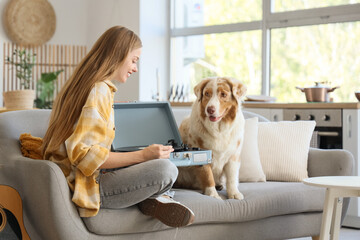 Wall Mural - Young woman with record player and Australian Shepherd dog sitting on sofa at home