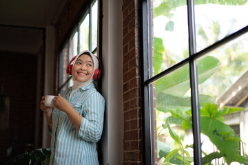 young Asian woman in hijab enjoying music using a headsets with a music player from her mobile phone while relaxing in a cafe, technology concept.
