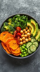 A vibrant bowl of fresh vegetables, avocado, and sweet potato with chickpeas for an eco-friendly meal on a gray background. The photo showcases the colorful arrangement of organic ingredients 