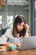 © Satori Studio - A young woman in a white blouse focuses intently on her laptop while sitting in a modern cafe, with a coffee and notebook on the table.