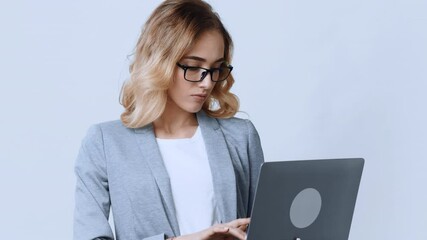 Poster - A young woman with wavy blonde hair and glasses focuses intently on her laptop while seated at a sleek desk in a contemporary office environment.