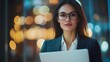 © sungedi - Woman in Glasses Holding a Laptop with Blurred City Lights in the Background