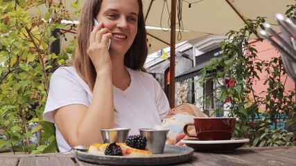 Wall Mural - Happy woman eating delicious cheese pancakes with fresh blackberries enjoying tasty dessert in cozy cafe during breakfast while talking on smartphone and taking care of newborn baby