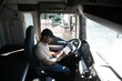 © Serhii - African-American truck driver is sitting behind the wheel holding a clipboard and checking the documents for the cargo