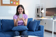 © crizzystudio - Happy young woman relaxing on sofa at home using mobile phone to text, chat, online, chat, video call. Attractive young woman looks at wireless internet on device. Shopping online from home.