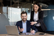 © Liubomir - Colleagues engaging in business meeting, discussing project ideas in office. Man in suit working on laptop, woman pointing at documents. Professional teamwork highlights collaboration