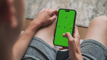 Poster - teenage boy uses mobile phone with green screen mockup, surfs the internet or scrolls social media w