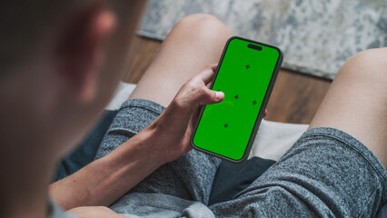 Poster - teenage boy uses mobile phone with green screen mockup, surfs the internet or scrolls social media w